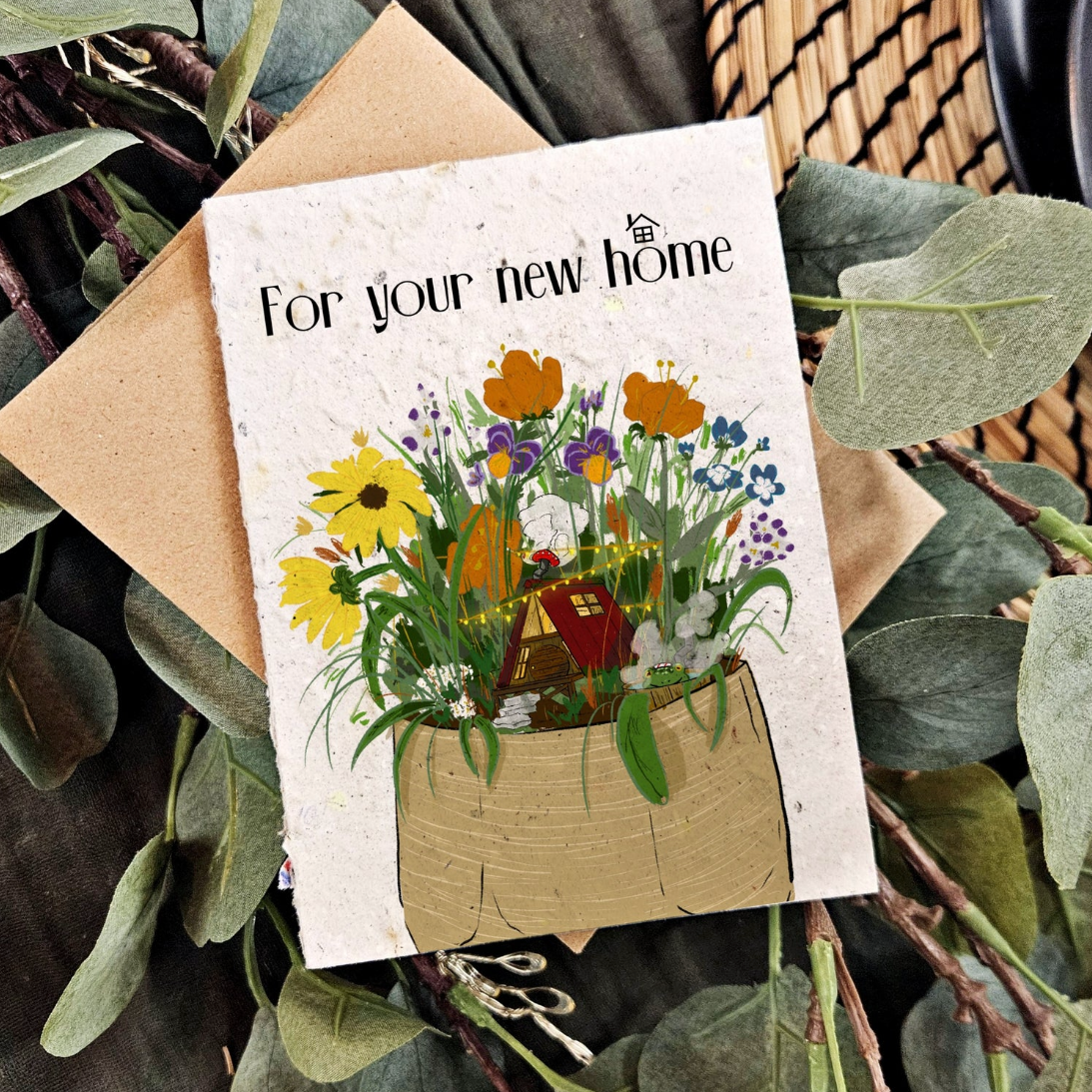 Plantable greeting card with a wildflower planter. In the planted is a magical little a-frame home. At the top is 'For your new home' text. 